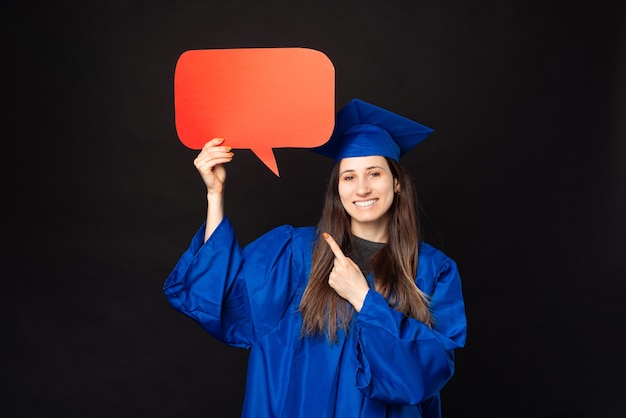 Enthousiaste jeune femme étudiante en robe bleue l'obtention du diplôme et pointant sur la bulle de dialogue