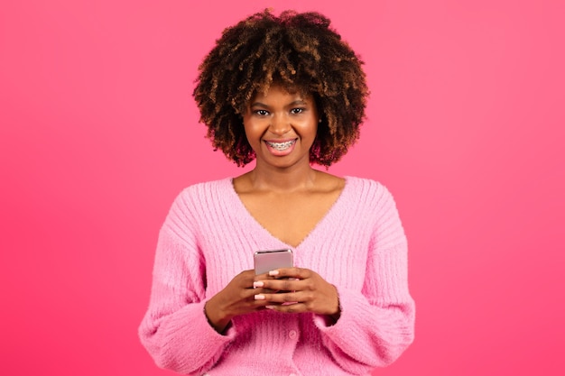 Enthousiaste jeune femme frisée noire décontractée avec des accolades en tapant sur un smartphone lire un message