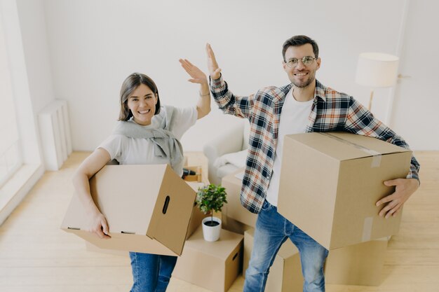 Enthousiaste jeune femme et homme donner haut cinq, sourire agréablement à la caméra, vêtu de vêtements décontractés, commencer une nouvelle vie