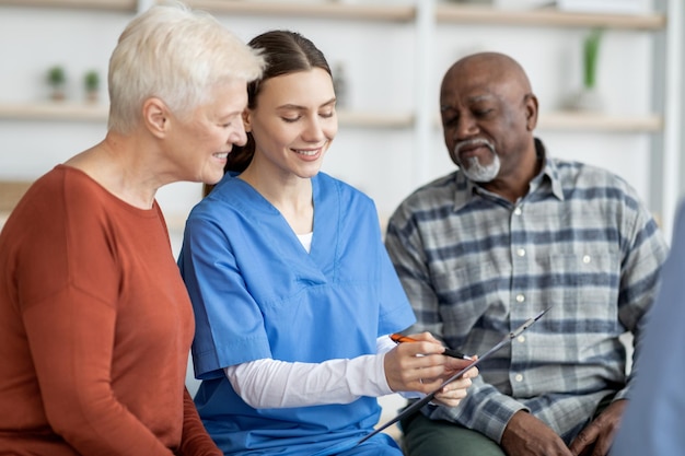 Enthousiaste jeune femme médecin ayant une conversation avec des personnes âgées