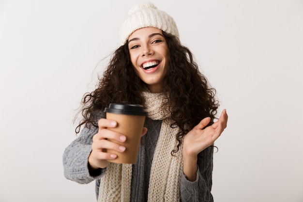 Enthousiaste jeune femme portant un foulard d'hiver debout isolé sur un mur blanc, tenant une tasse de café à emporter