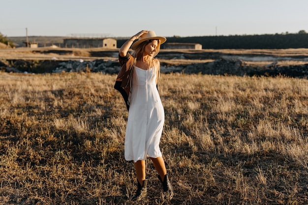 Enthousiaste jeune femme portant une robe vintage et un chapeau de paille dans une ferme