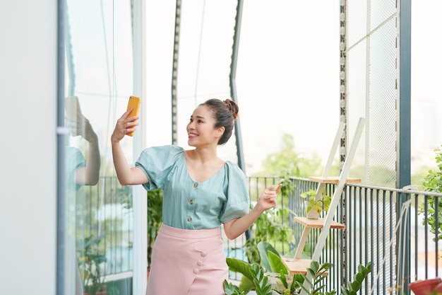 Enthousiaste jeune fille asiatique ayant un appel vidéo avec son téléphone lorsqu'elle se tient sur le balcon