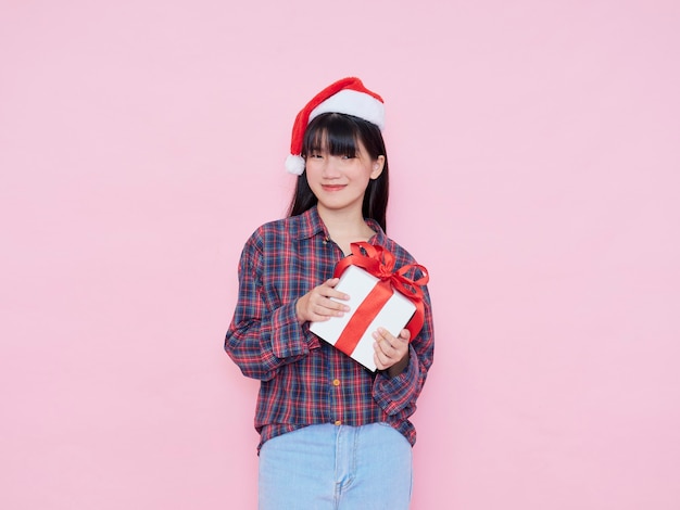 Enthousiaste jeune fille portant bonnet de Noel avec boîte-cadeau sur fond rose