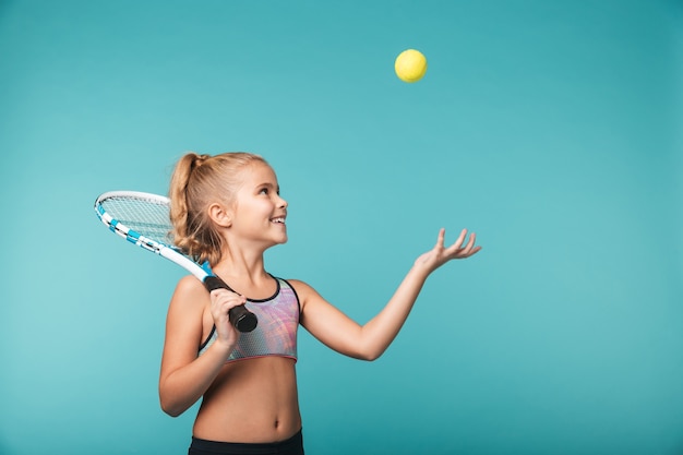 Enthousiaste jeune fille sportive jouant au tennis isolé sur mur bleu