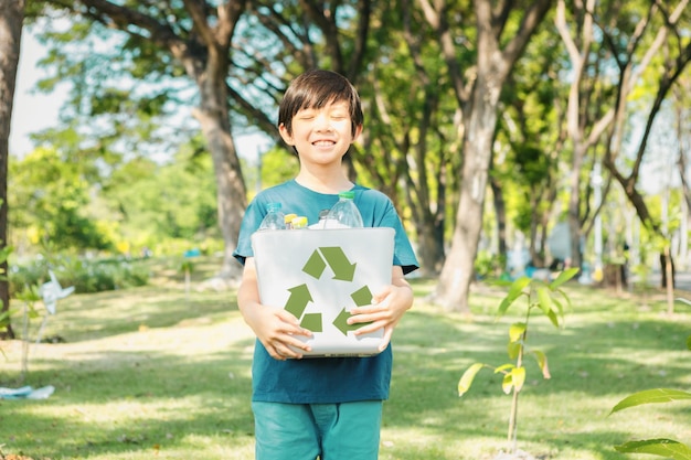 Enthousiaste jeune garçon asiatique tenant une corbeille de recyclage dans un parc vert naturel à la lumière du jour favorisant le recyclage des déchets, réduisant et réutilisant les encouragements pour une sensibilisation éco-durable pour la génération future Gyre