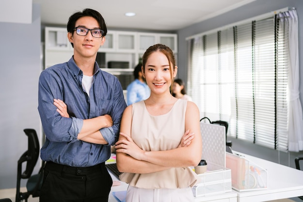 Enthousiaste jeune homme d'affaires asiatique portant des lunettes et une femme d'affaires décontractée souriant et regardant la caméra tout en se tenant les bras croisés