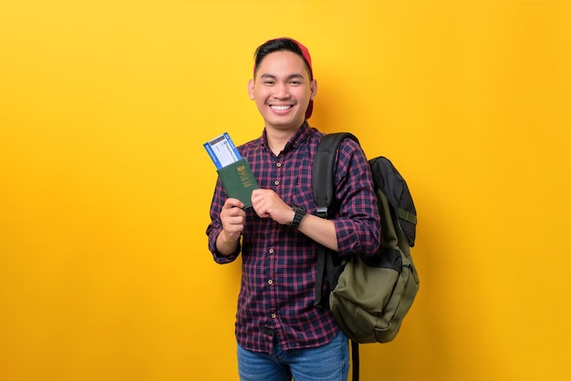 Enthousiaste jeune homme asiatique avec sac à dos tenant un passeport et des billets d'avion isolés sur fond jaune Concept de tourisme et de voyage de vacances
