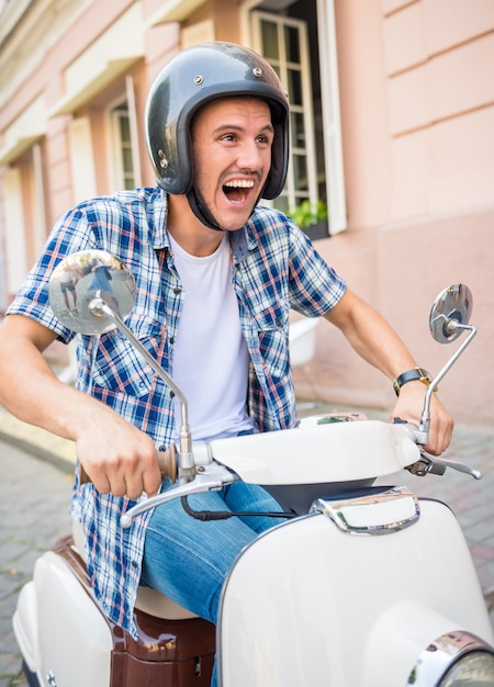 Enthousiaste jeune homme au casque monte sur un scooter en ville.