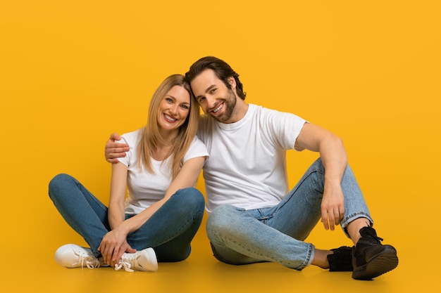 Enthousiaste jeune homme européen séduisant avec barbe et femme étreignant assis sur le sol isolé sur jaune