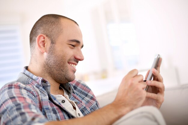 Enthousiaste jeune homme à la maison à l'aide de smartphone