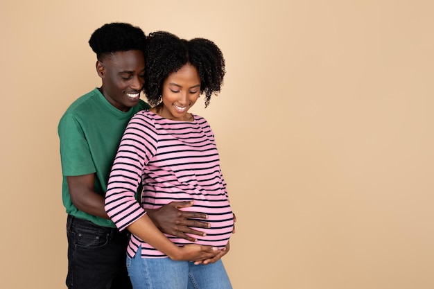 Enthousiaste jeune homme noir étreignant dame avec gros ventre sentir le mouvement du bébé profiter de la grossesse et