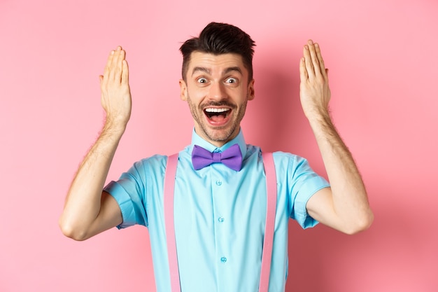 Enthousiaste jeune homme ouvre les yeux pour un cadeau surprise lors de la célébration de vacances, à la surprise de cadeau, debout sur le rose.