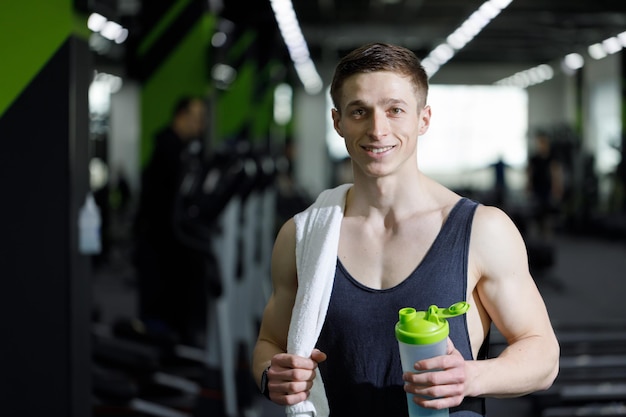 Enthousiaste jeune homme de remise en forme avec une serviette et une bouteille d'eau marchant sur l'entraînement en salle de sport