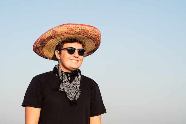 Enthousiaste jeune homme en sombrero en fond de ciel clair. Mexique concept de fête de l'indépendance de l'homme portant un chapeau mexicain national et un bandana de style occidental