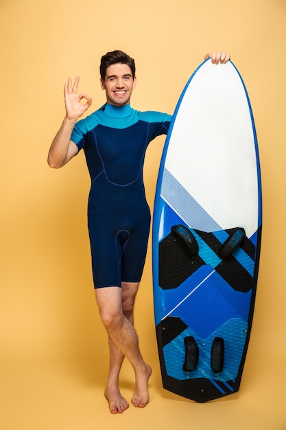 Enthousiaste jeune homme tenant la planche de surf faire un geste correct.