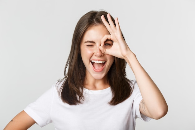 Enthousiaste jolie fille souriante et montrant un geste correct, un clin d'œil excité.