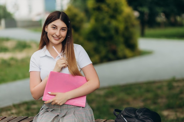 Enthousiaste jolie jeune femme avec sac à dos et cahiers debout et souriant dans le parc