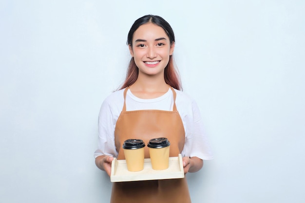 Enthousiaste jolie jeune fille barista en tablier donnant une tasse de café à emporter isolé sur fond blanc