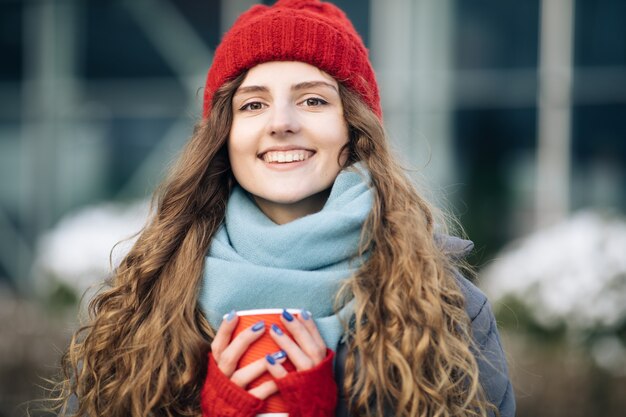 Enthousiaste magnifique brune bouclée en mode hiver tenant une tasse de café sur urbain