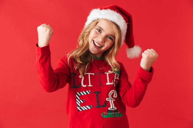Enthousiaste petite fille portant le costume de Noël debout isolé