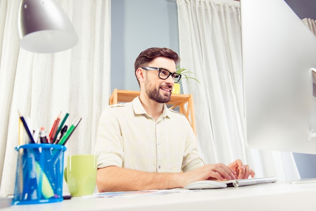 Enthousiaste pigiste dans des verres travaillant avec pc et tapant au bureau