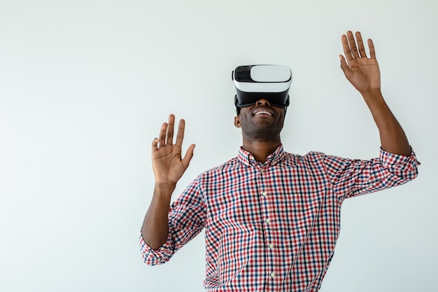 Enthousiaste ravi homme afro-américain souriant et testant des lunettes vr contre un mur blanc