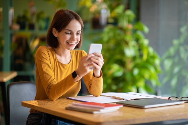 Enthousiaste séduisante jeune femme brune à l'aide de téléphone au café