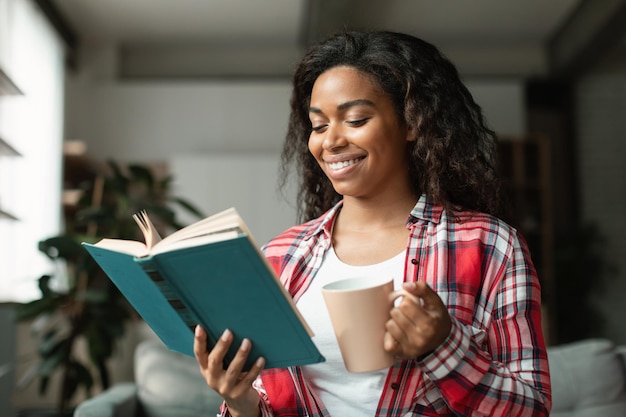Enthousiaste smart jolie jeune femme noire étudiant lisant un livre profitez d'une tasse d'étude de boisson chaude préférée