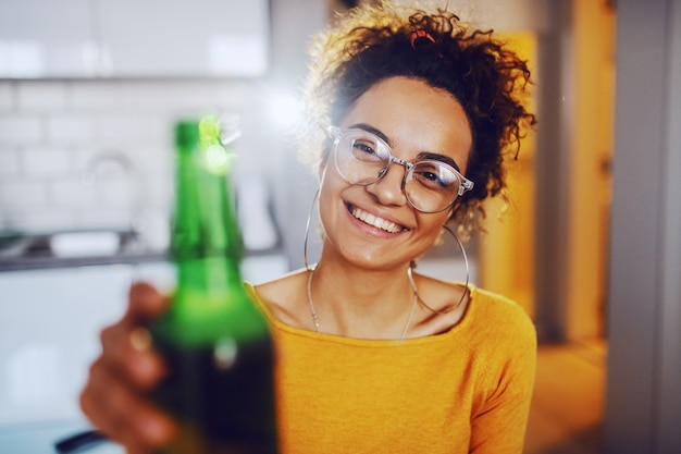 Enthousiaste souriante brune caucasienne bronzée mignonne aux cheveux bouclés assis à la fête et grillage avec de la bière.