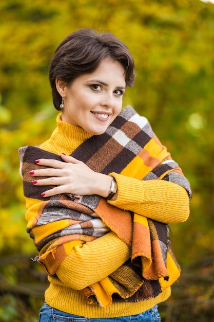 Enthousiaste souriante jeune brune enveloppée dans une couverture dans la forêt d'automne