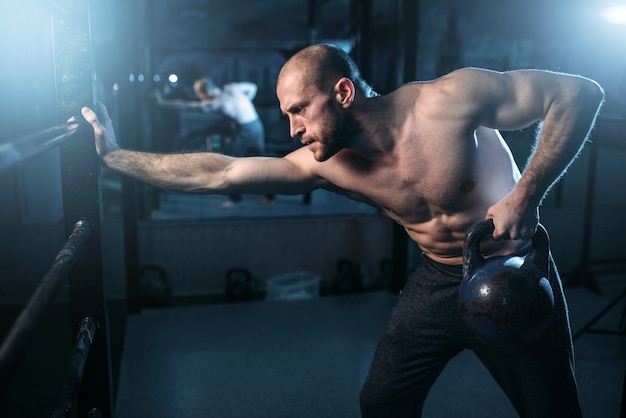 Entraînement d'athlète musculaire, homme soulevant kettlebell. Entraînement sportif fort avec poids