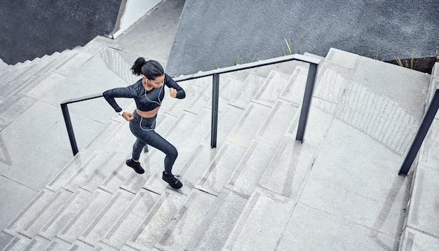 Entraînement au-dessus et femme courant dans les escaliers pour les sports motorisés et l'énergie corporelle dans la ville Exercice de défi et coureur d'athlète avec cardio sur les marches pour un marathon santé et performance d'entraînement