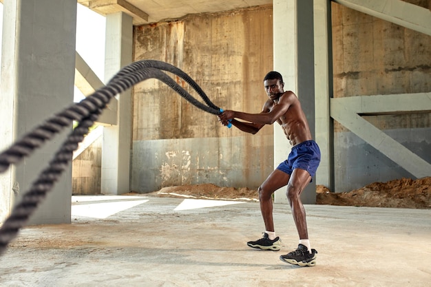 Entraînement de corde Sport homme faisant des cordes de combat exercice en plein air Athlète masculin noir faisant de l'exercice de conditionnement physique fonctionnel avec une corde lourde