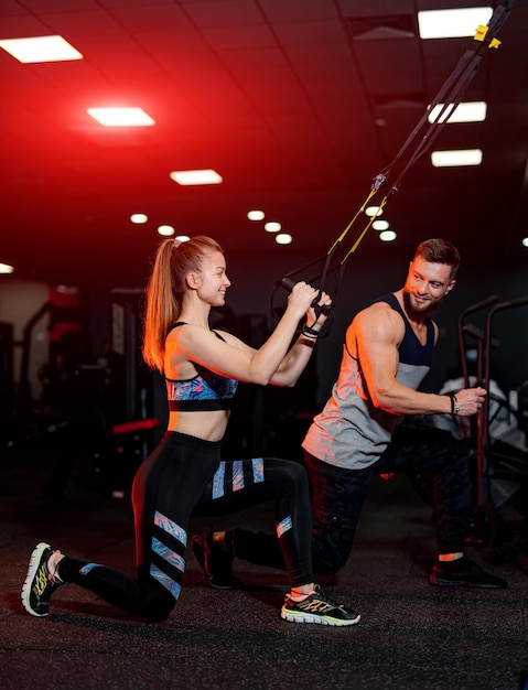 Entraînement de couple sportif dans la salle de gym. Jeune entraîneur personnel athlétique aidant son client.