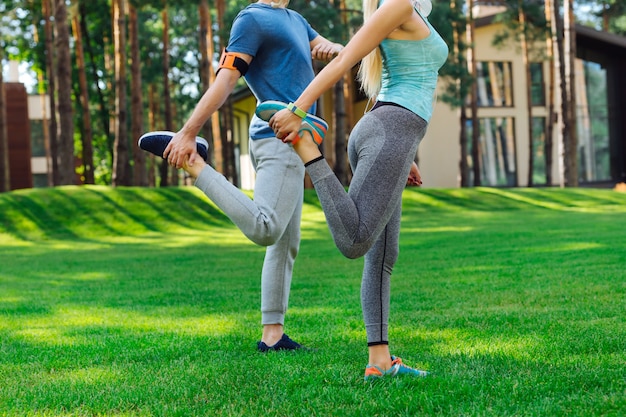 Entraînement de fitness. Beaux jeunes debout ensemble sur l'herbe tout en faisant un exercice d'étirement