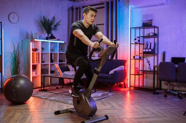 Entraînement de fitness à domicile jeune homme asiatique athlète s'entraînant sur un vélo stationnaire intelligent à l'intérieur