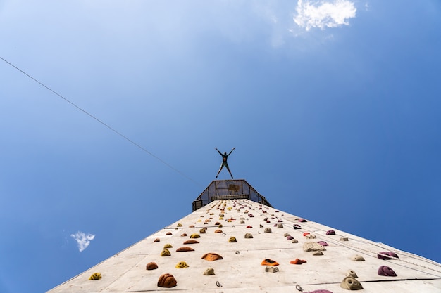 Entraînement de grimpeur sportif en plein air avec ciel bleu, escalade sur une paroi rocheuse colorée artificielle