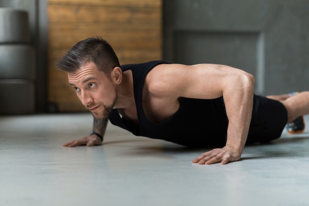 Entraînement de jeune homme dans un club de remise en forme. Closeup portrait of caucasian guy faisant planche ou push ups exercice, formation à l'intérieur