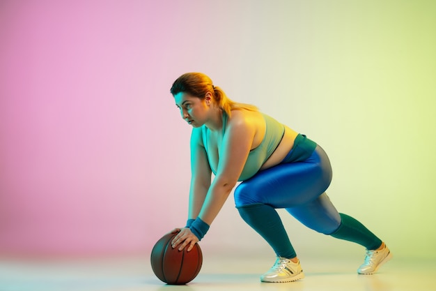 Entraînement d'un jeune modèle féminin de taille plus caucasienne sur un mur vert violet dégradé