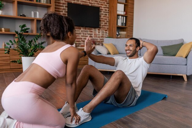 Entraînement à la maison Souriant jeune homme afro-américain et dame en tenue de sport faisant des exercices abdominaux toucher les mains