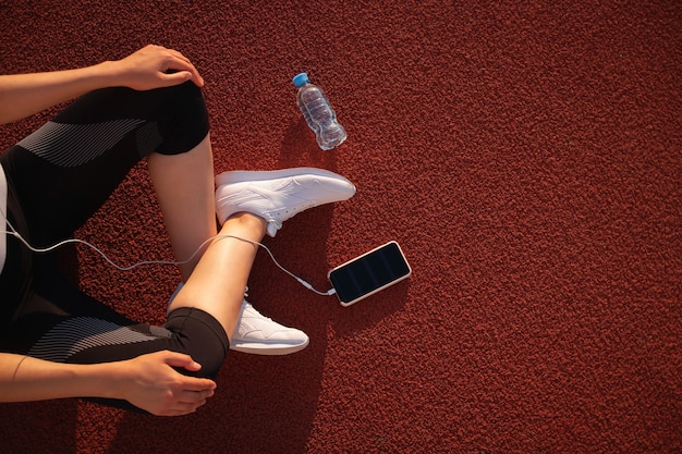 Entraînement et remise en forme dans le stade. La fille du coureur tient un smartphone à l'aide d'un écran tactile pour sélectionner de la musique ou du texte sur l'application avant de se lancer sur la bonne voie.