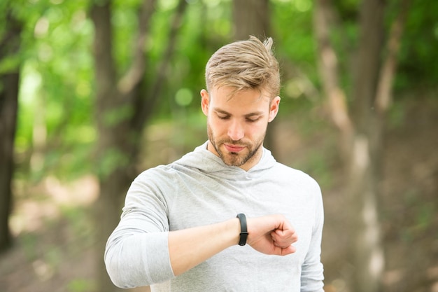 Entraînement sportif avec gadget podomètre. Athlète de l'homme sur le tracker de remise en forme de contrôle de visage occupé, fond de nature. Athlète à poils avec tracker de fitness ou podomètre. Concept de gadgets sportifs.