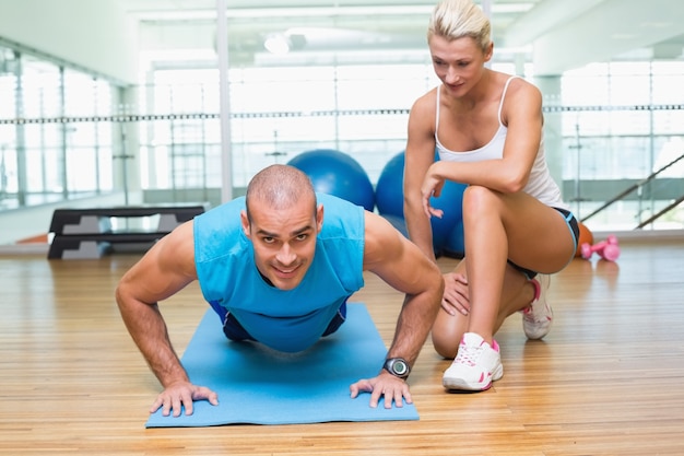 Entraîneur aidant l&#39;homme avec des push ups au gymnase