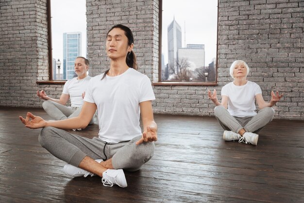 Entraîneur asiatique gardant les yeux fermés mettant les mains sur les genoux tout en étant détendu