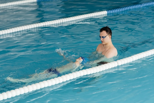 Un entraîneur enseigne à un garçon de sept ans à nager dans une piscine moderne Apprendre à nager Développement des sports pour enfants Parentalité saine et promotion des sports pour enfants