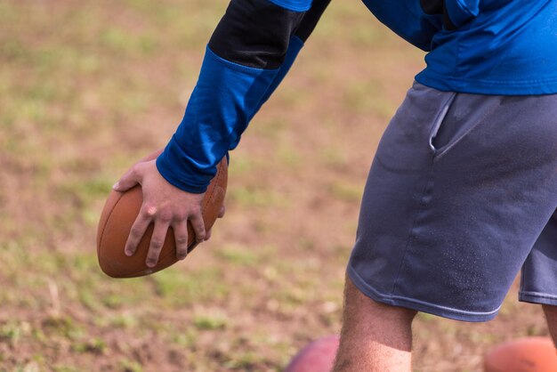 Entraîneur d'équipe lançant le ballon dans le groupe de jeunes joueurs de football américain en action pendant l'entraînement sur le terrain