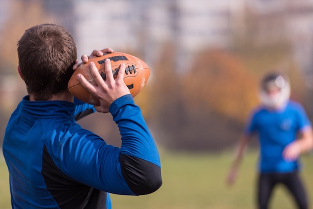 Entraîneur d'équipe lançant le ballon dans le groupe de jeunes joueurs de football américain en action pendant l'entraînement sur le terrain