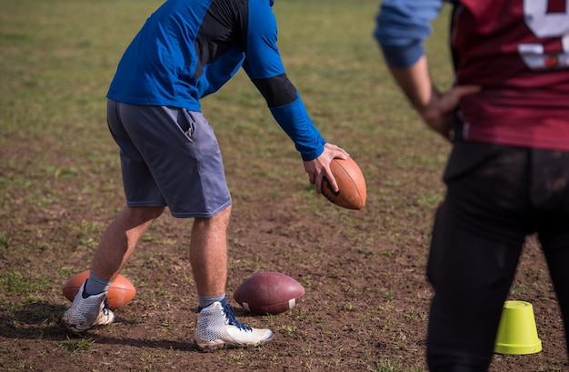 Entraîneur d'équipe lançant le ballon dans le groupe de jeunes joueurs de football américain en action pendant l'entraînement sur le terrain