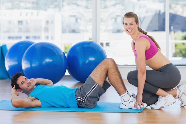 Entraîneur féminin aidant l&#39;homme avec ses exercices au gymnase